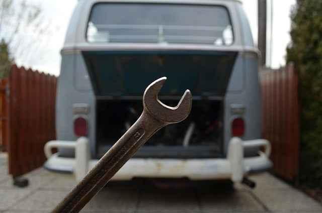 Close-up of a wrench in front of an open rear engine compartment of a vintage grey van in an outdoor setting