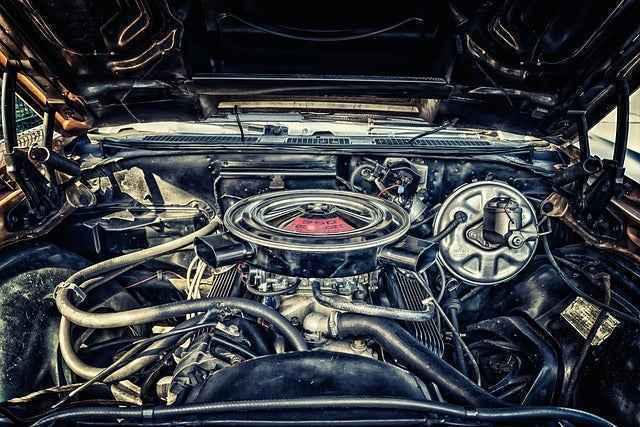 Open car hood showing detailed vintage vehicle engine with hoses and air filter in engine bay