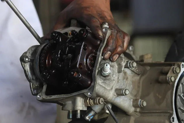 Mechanic's hand working on disassembled car engine cylinder head with visible valves and spark plug